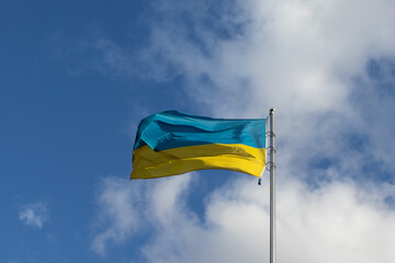 Ukrainian yellow and blue flag on a flagpole waving in the wind against a bright blue sky with white clouds outside. Independence Day, Constitution Day, a symbol of freedom, democracy, and victory
