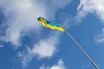 Ukrainian yellow and blue flag on a flagpole waving in the wind against a bright blue sky with white clouds outside. Independence Day, Constitution Day, a symbol of freedom, democracy, and victory
