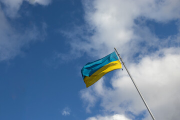 Ukrainian yellow and blue flag on a flagpole waving in the wind against a bright blue sky with white clouds outside. Independence Day, Constitution Day, a symbol of freedom, democracy, and victory