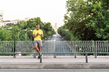 Sporty adult man using cellphone on sidewalk in the footbridge outdoors