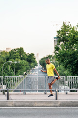 Fototapeta na wymiar Adult man stretching his leg holding phone in the footbridge at day