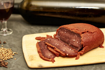 sliced basturma on a plate next to a bottle of wine and a glass
