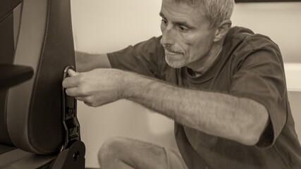 Obraz premium Man assembling new furniture at home, new purchase, hobby concept. Caucasian male mounting a gaming chair