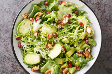 Fresh healthy salad with kale, Brussels Sprouts Pomegranate, Avocado, walnuts and lettuce closeup in the bowl on the table. Horizontal top view from above