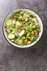 Fresh salad consisting of Brussels sprouts, avocado, cabbage, lettuce, pomegranate and nuts close-up in a plate on the table. Vertical top view from above