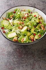 Fresh salad consisting of Brussels sprouts, avocado, cabbage, lettuce, pomegranate and nuts close-up in a plate on the table. Vertical