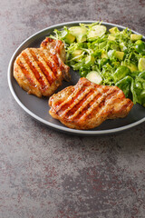 Grilled pork chops and green vegetable salad with brussels sprouts, avocado and herbs closeup in the plate on the table. Vertical