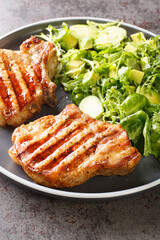 Grilled pork steak and green vegetable salad closeup in the plate on the table. Vertical