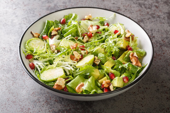 Dietary raw vegetable salad of brussels sprouts, avocado, cabbage, lettuce, pomegranate and nuts close-up in a plate on the table. horizontal