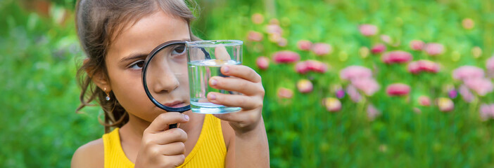 The child examines a glass of water with a magnifying glass. Selective focus.