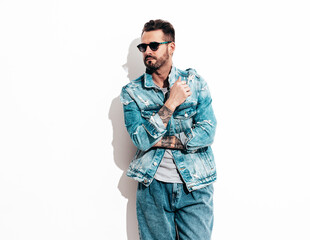 Portrait of handsome confident stylish hipster lambersexual model. Sexy man dressed in jeans jacket. Fashion male isolated on white in studio. In sunglasses