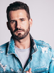 Portrait of handsome confident stylish hipster lambersexual model. Sexy man dressed in jeans jacket. Fashion male isolated on grey wall in studio