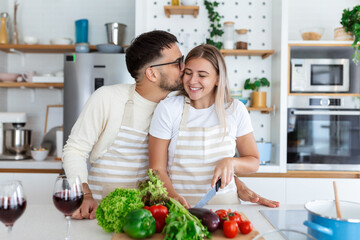 happy young couple have fun in modern kitchen indoor while preparing fresh fruits and vegetables food salad. Beautiful young couple talking and smiling while cooking healthy food in kitchen at home.