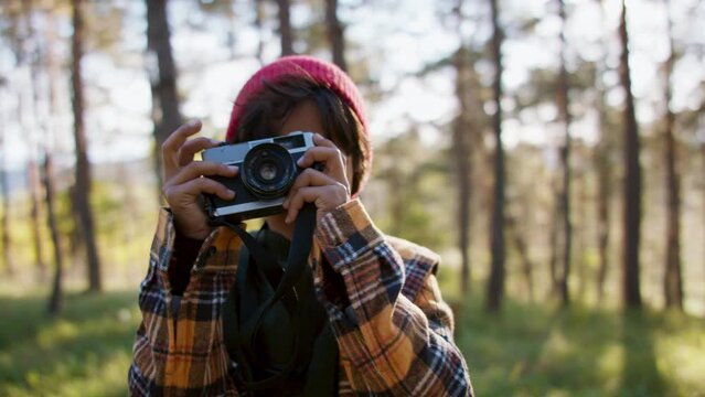 Little multiracial boy taking photos at old camera in the middle of forest in autumn.