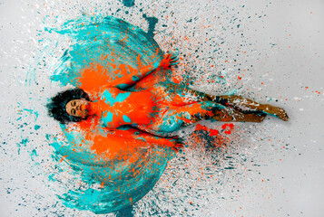 top view to sexy naked woman lying elegant on the floor in turquoise blue orange color abstractly painted bodypainting girl on splashed ground