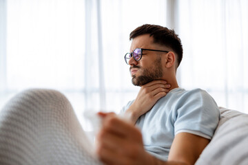 Sick man lying on the couch with high temperature and holding his throat with hand.