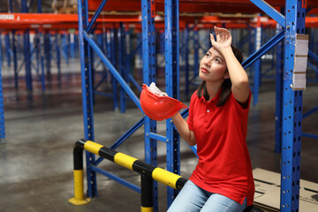 Fototapeta premium Portrait of warehouse workers young asian woman sitting and taking a break while wipe the sweat away after controlling stock and inventory in retail warehouse logistics, distribution center