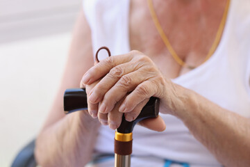 Elderly pensioner holding hands on wooden cane closeup