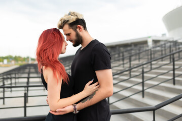 Stylish couple in love in black clothes walks in the park and hugs. Lovely couple of hipsters hugging on the background of the stairs. Youth, love and lifestyle concept