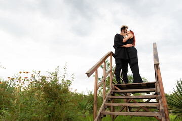 Stylish couple in love in black clothes walks in the park and hugs. A lovely couple of hipsters are standing on a wooden bridge and kissing. Youth, love and lifestyle concept
