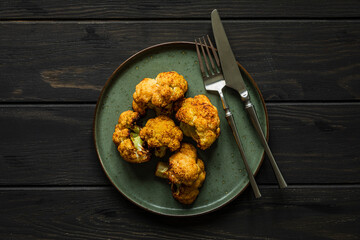 Baked seasoned cauliflower served on a plate with knife and fork on wooden backdrop