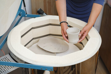 close-up of hands putting vase into the kiln, oven for roasting of unbaked clay handmade products,...