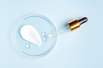 smear of cream stroke and round transparent drop of gel serum in a petri dish on a blue background. Concept laboratory tests and research, making and testing cosmetic
