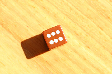 A brown dice with the number six on it on a wooden table