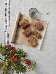 The cupcake is cut into pieces and lies on parchment. Vanilla and chocolate cake. Top view, in composition with bunches of mountain ash. Autumn mood.