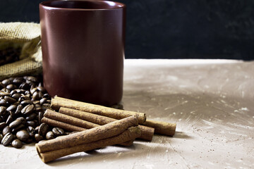 coffee beans spilled out of a canvas bag of cinnamon and a coffee mug onto a table with a place of copispace