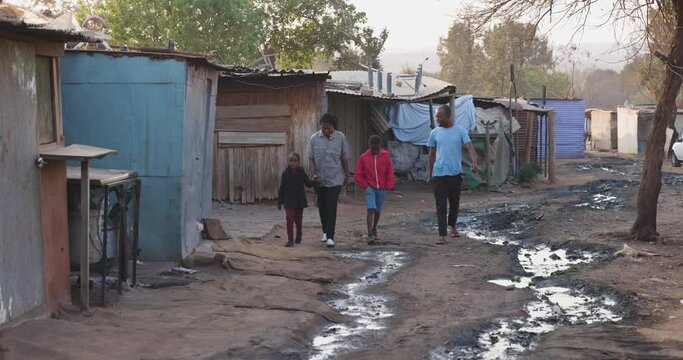 Poverty. Inequality. Poor Black African family walking in a typical slum area showing poverty of surroundings and water waste in Africa