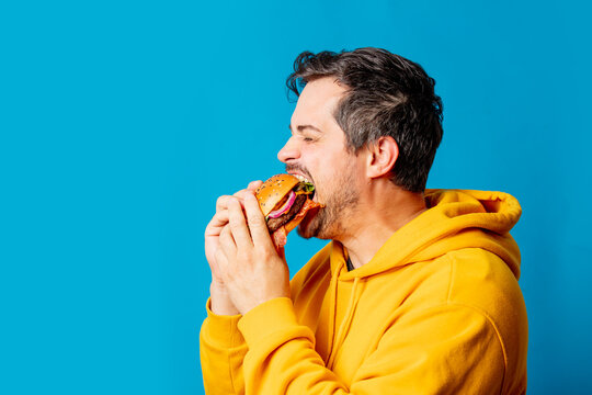  white guy in yellow hoodie eating hamburger on blue background