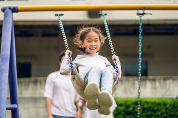 Obraz premium Portrait of enjoy happy love asian family father and mother with little asian girl smiling playing and pushing daughter on the swing moments good time at playground