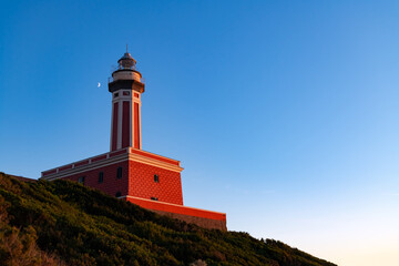 Red Lighthouse “Faro Di Punta Carena“ on the south west end of Capri Italy with moon and warm...