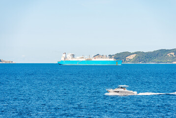 Blue and white liquefied natural gas tanker ship and a motorboat in the Mediterranean Sea, Gulf of La Spezia, Liguria, Italy, Europe. On background the Palmaria and Tino islands, Porto Venere.