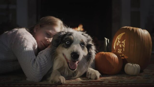Girl with a dog is resting by a burning fireplace, next to Halloween decorations
