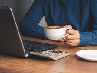 Businessman hand holding a cup of coffee sitting working at the office