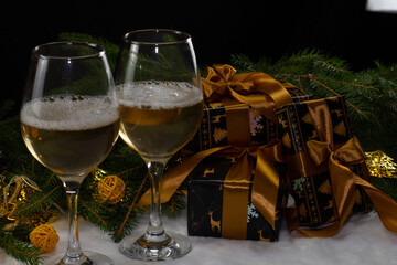 A pile of Christmas gifts in black wrapping and gold ribbon lie near champagne flutes, fir branches and yellow balls Festive atmosphere of Christmas and New Year.