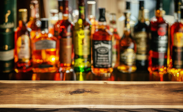 Wooden table top and beautiful bokeh shelves with alcohol bottles at the pub background. Bar concept.