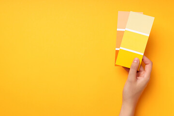 Female hand holding color palettes on yellow background