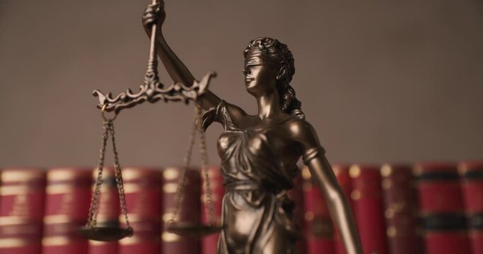 close up of law statue blindfolded lady with a scale in her hands for two broad sources of law in front of books in a university room