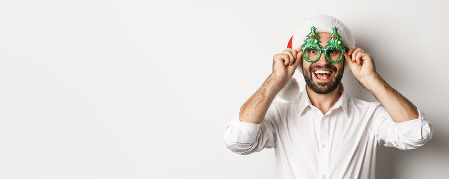 Close-up of happy man celebrating christmas holidays, wearing party glasses and santa hat, enjoying New Year, white background