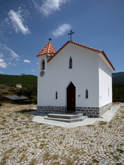 Chapelle traditionnelle blanche à toit en tuiles oranges et tour clocher sur la place d'un village typique du centre du Portugal.