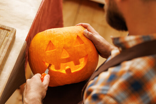 Cropped shot of  man carving large orange pumpkin while preparing for Halloween party