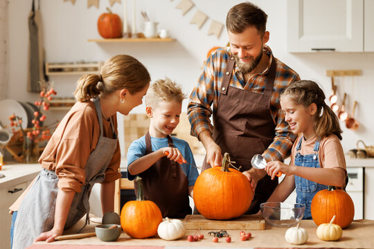 Happy family mother, father and kids  to remove pulp from from pumpkin while carving jack o lantern with family