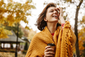 Funny young fair-skinned brown-haired lady laughs with her head tilted in fresh air. Girl wrapped...