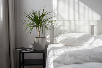 Minimalistic modern bedroom with white bedding and grey curtains. Morning light from the window falling on a bed with white satin bedding.