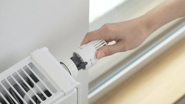 The woman turns the regulator of the thermostatic valve of the radiator to increase the temperature of the heater in the room to the maximum. Heating of the apartment in cold weather and severe frosts