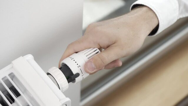 The man turns off the heating by setting the regulator of the thermostatic valve of the radiator to the minimum value. Turning off the heating in the apartment during the energy crisis.