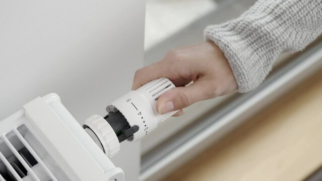 The woman turns the regulator of the thermostatic valve of the radiator to increase the temperature of the heater in the room to the maximum. Heating of the apartment in cold weather and severe frosts